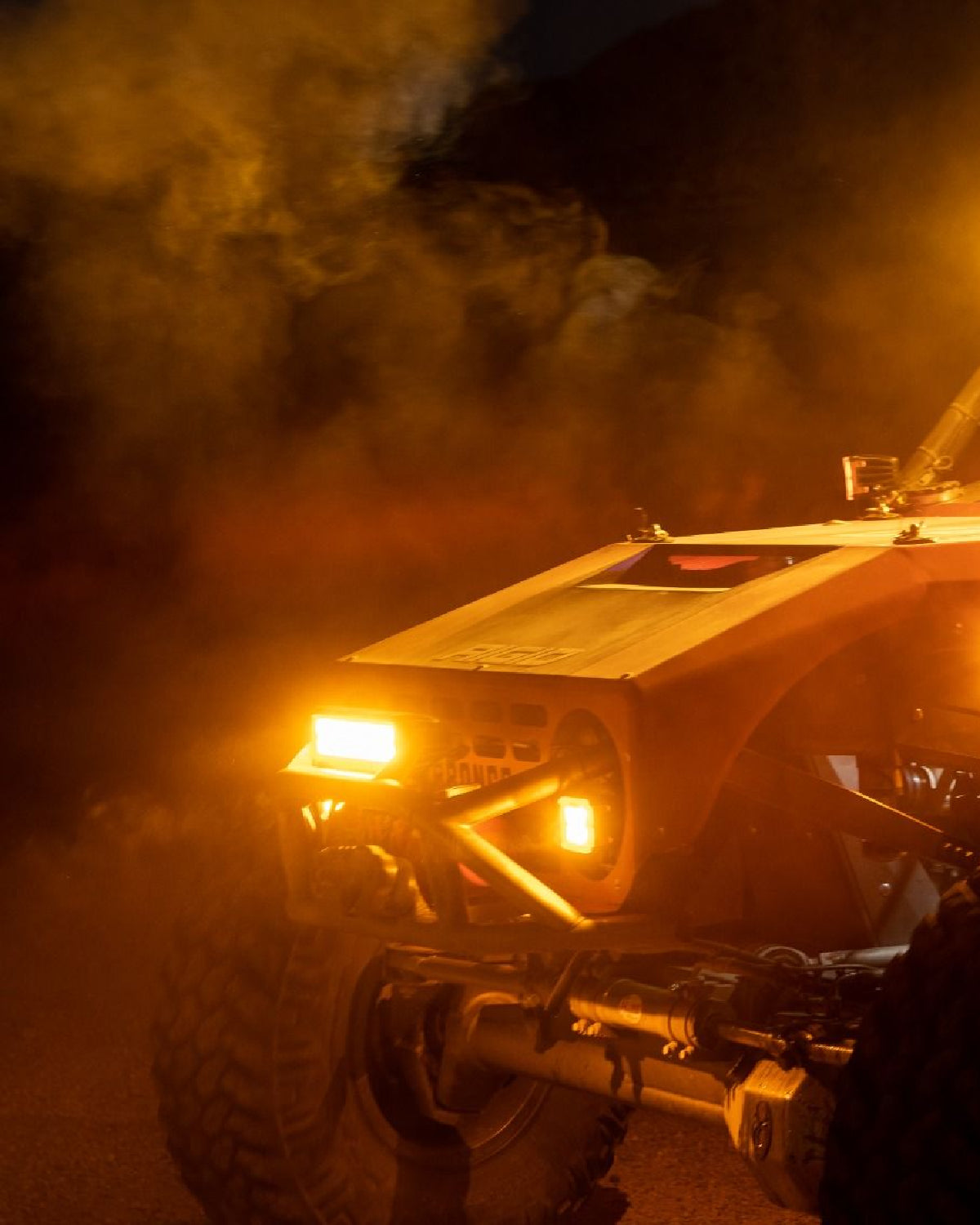 Off-road vehicle with glowing headlights in a dusty, orange-lit environment